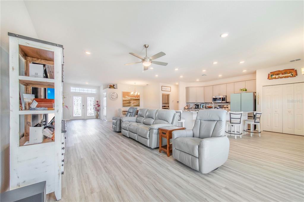 An open-concept living room features light wood-look flooring, a grey sofa set, and a kitchen — 1096 SANDPIPER LOOP, WINTER HAVEN, FL