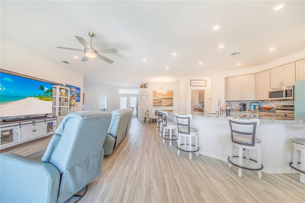 An open-concept living room and kitchen featuring light wood flooring, a large television, and barstools — 1096 SANDPIPER LOOP, WINTER HAVEN, FL