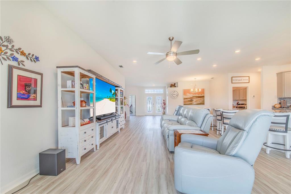 A living room features light wood-look flooring, a large television unit, and light-colored leather seating — 1096 SANDPIPER LOOP, WINTER HAVEN, FL