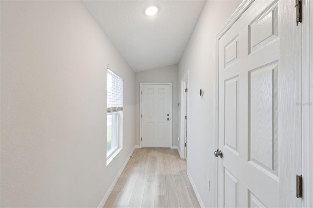 A bright hallway features light wood-look flooring, white walls, and a white entry door — 4015 GARDENIA AVENUE, HAINES CITY, FL