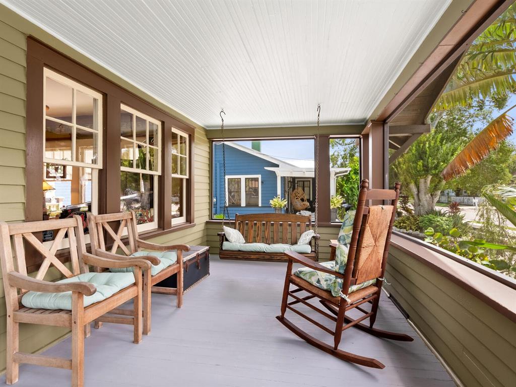 A covered porch features wooden furniture, a hanging swing, and views of a blue house — 2322 7TH AVENUE W, BRADENTON, FL