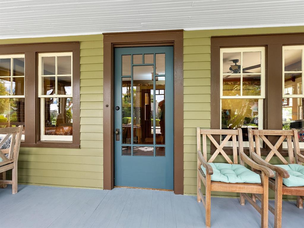 A front porch features a blue door, brown trim, olive siding, and wooden chairs — 2322 7TH AVENUE W, BRADENTON, FL