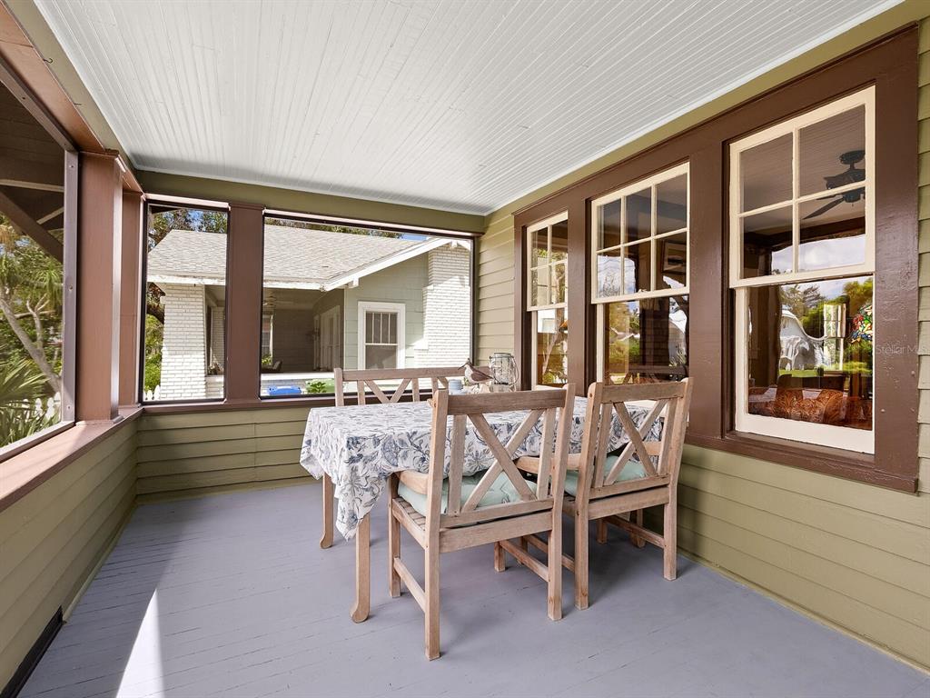 A covered porch features a dining table with chairs, wood siding, and large windows — 2322 7TH AVENUE W, BRADENTON, FL