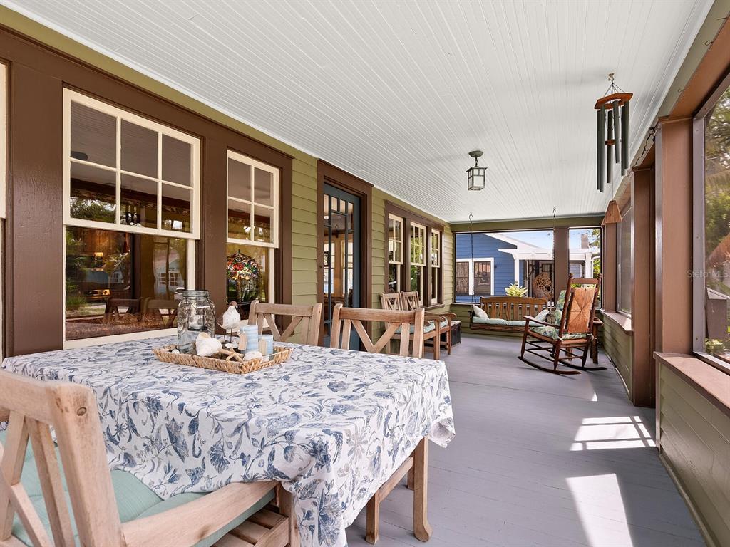 A covered porch features a dining table, a rocking chair, a hanging bench, and windows — 2322 7TH AVENUE W, BRADENTON, FL