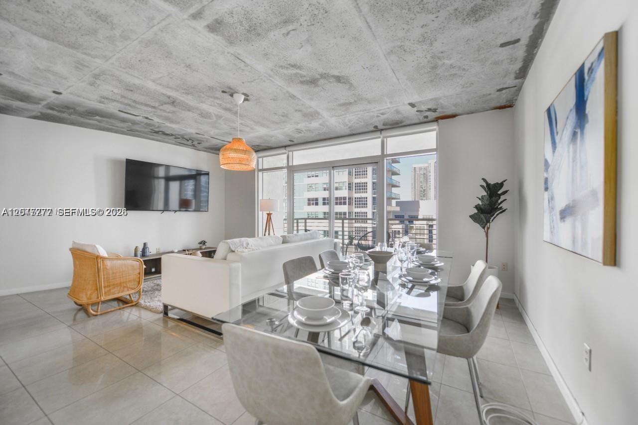 A modern living and dining area features a concrete ceiling, tile floors, and floor-to-ceiling windows — 3250 NE 1st Ave # 901, Miami FL 33137, MIAMI, FL