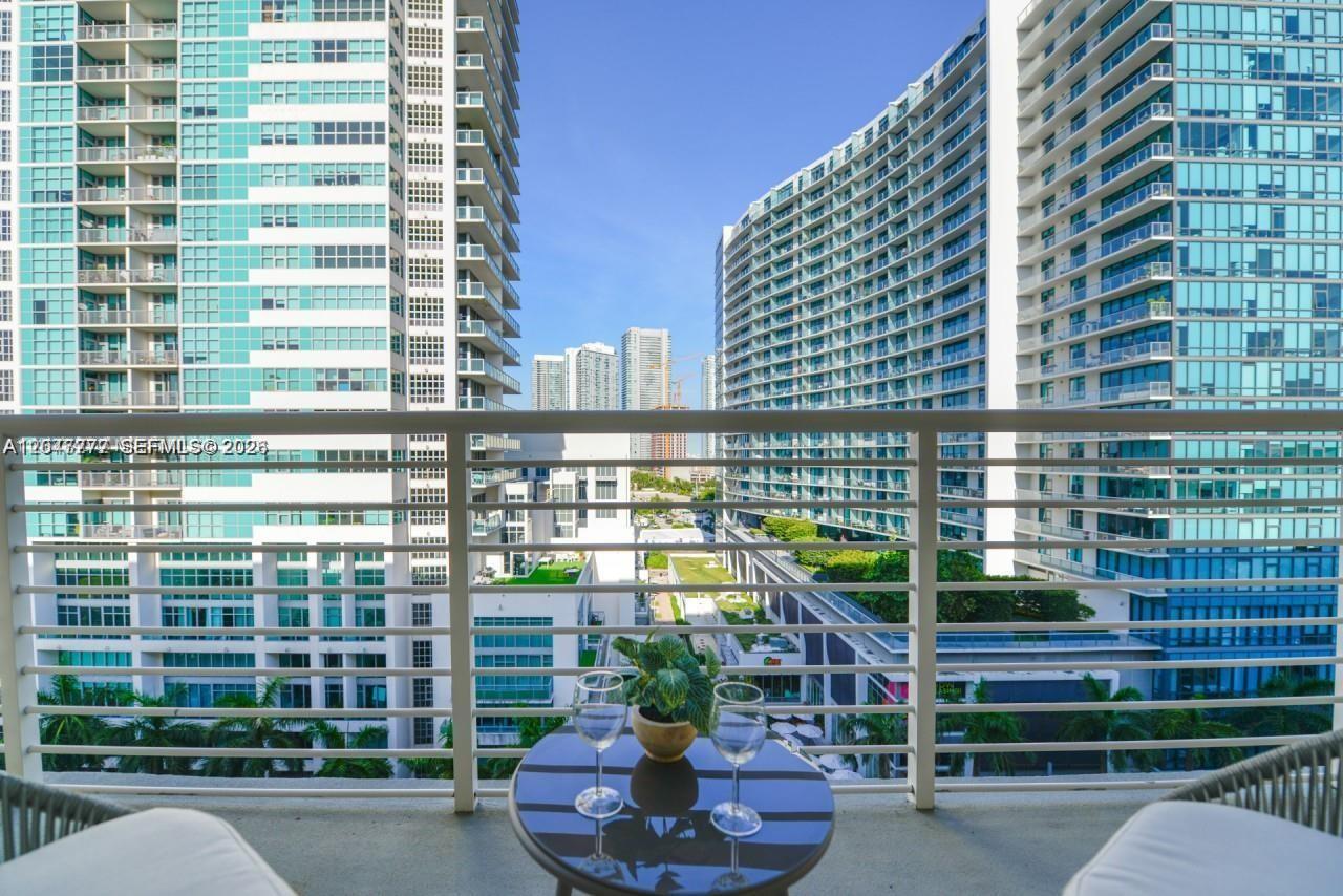 A balcony with a small table and two wine glasses overlooks a dense urban cityscape — 3250 NE 1st Ave # 901, Miami FL 33137, MIAMI, FL