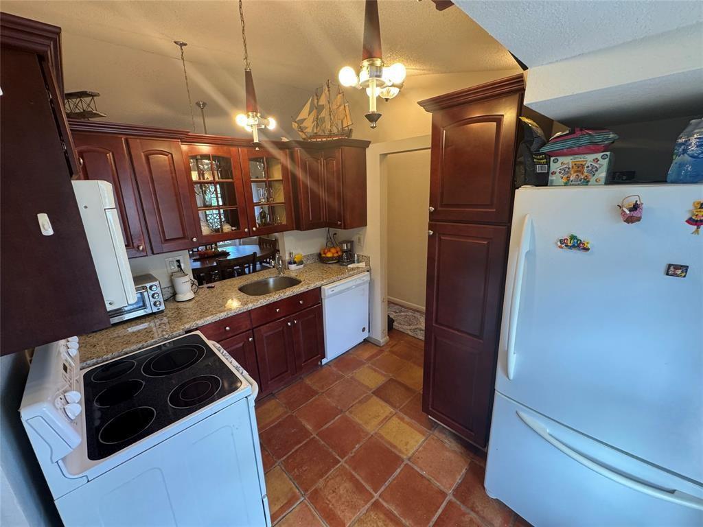 A kitchen features dark wood cabinets, granite countertops, a white stove, and terracotta tile flooring — 715 Gardens Drive # 203, Pompano Beach FL 33069, POMPANO BEACH, FL
