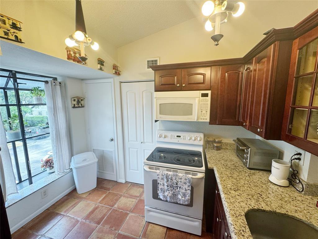 A kitchen features dark wood cabinets, granite countertops, a white stove, and terracotta tile flooring — 715 Gardens Drive # 203, Pompano Beach FL 33069, POMPANO BEACH, FL