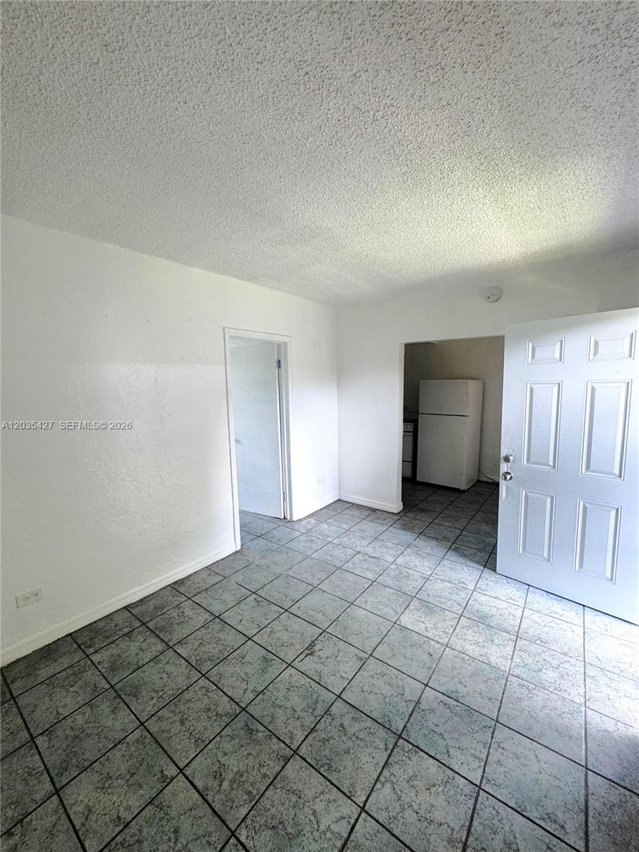 A room with white walls, a tiled floor, and an open doorway to a kitchen — MIAMI, FL