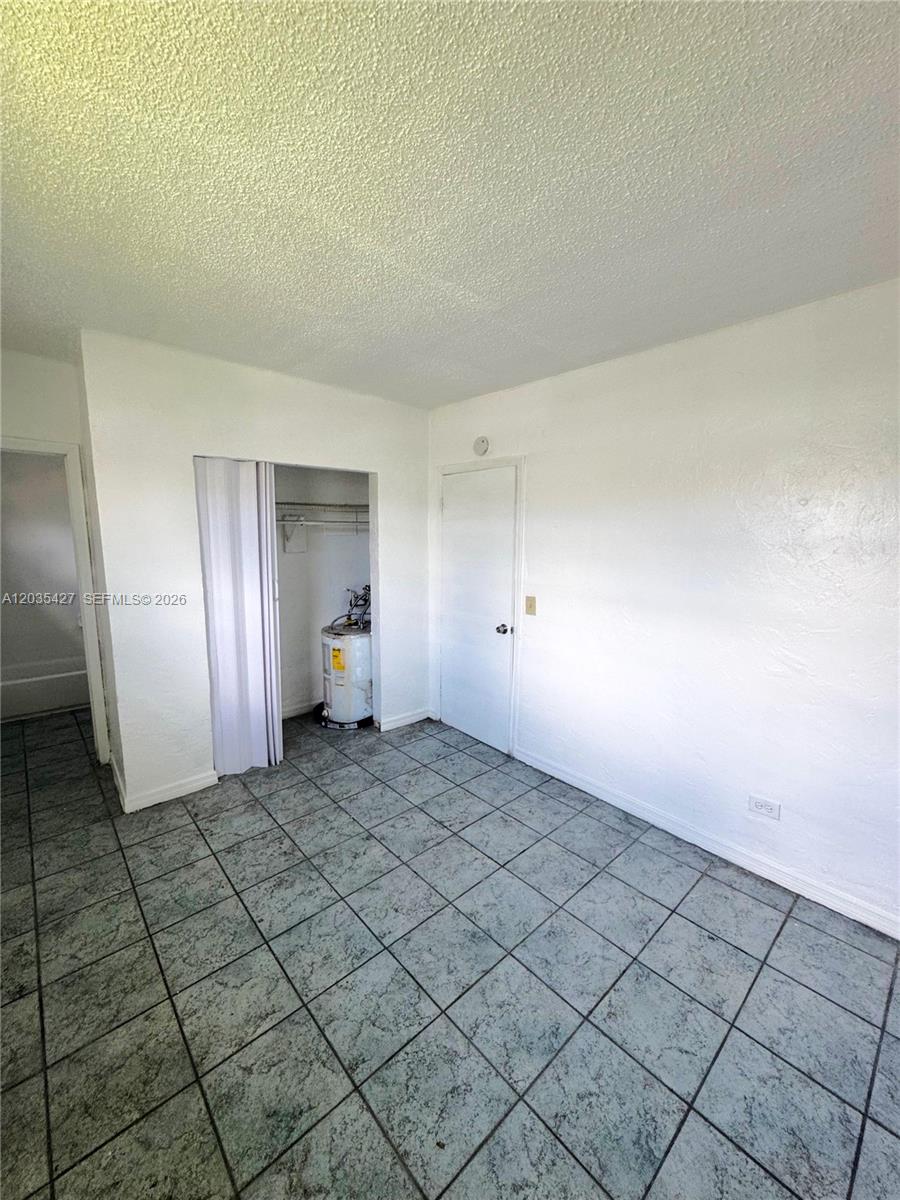 A room with tiled floors, a white door, and an open closet containing a water heater — MIAMI, FL