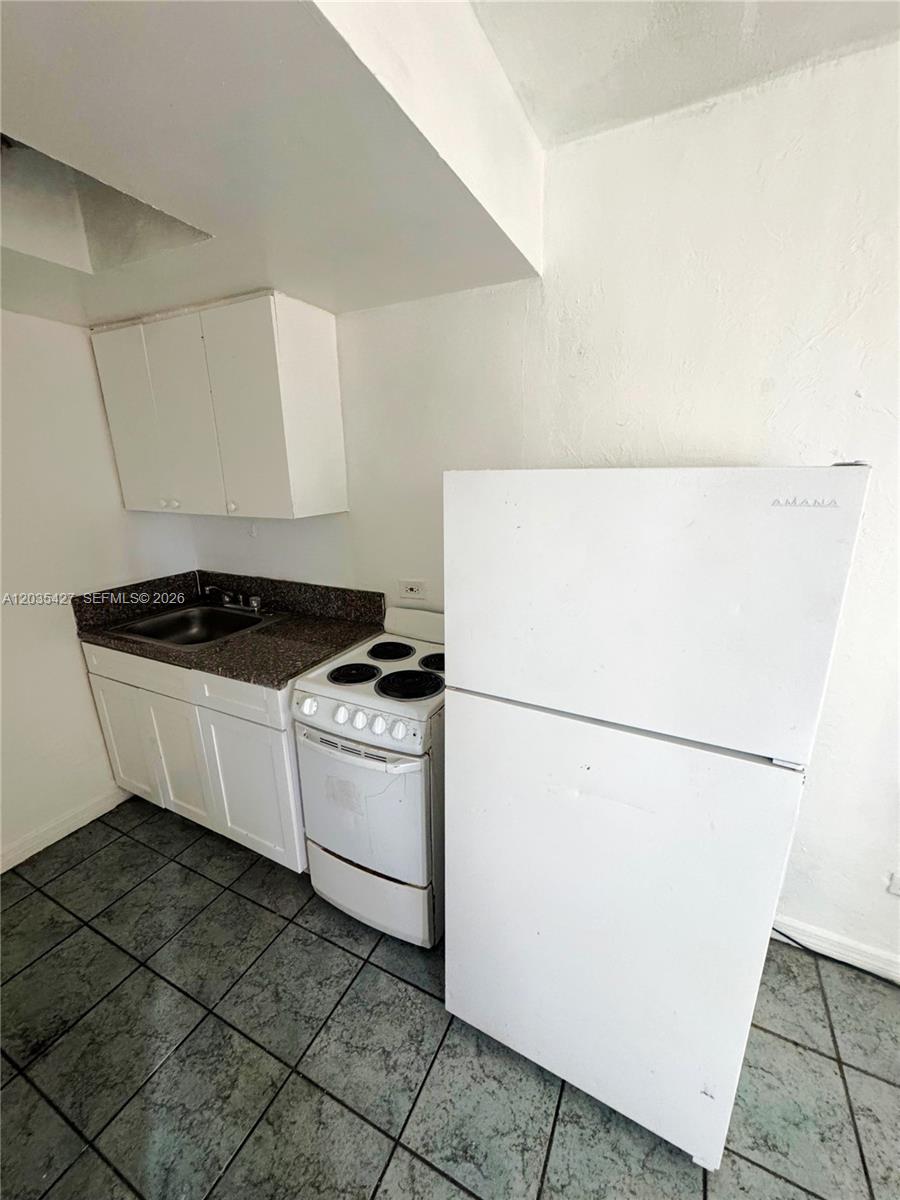 A small kitchen features white cabinets, a sink, a stove, and a white refrigerator — MIAMI, FL