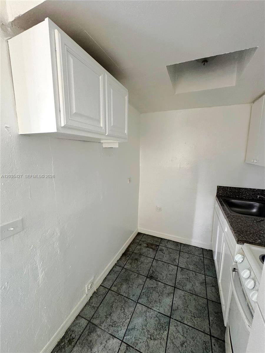 A small kitchen features white cabinets, dark granite countertops, and grey tiled flooring — MIAMI, FL