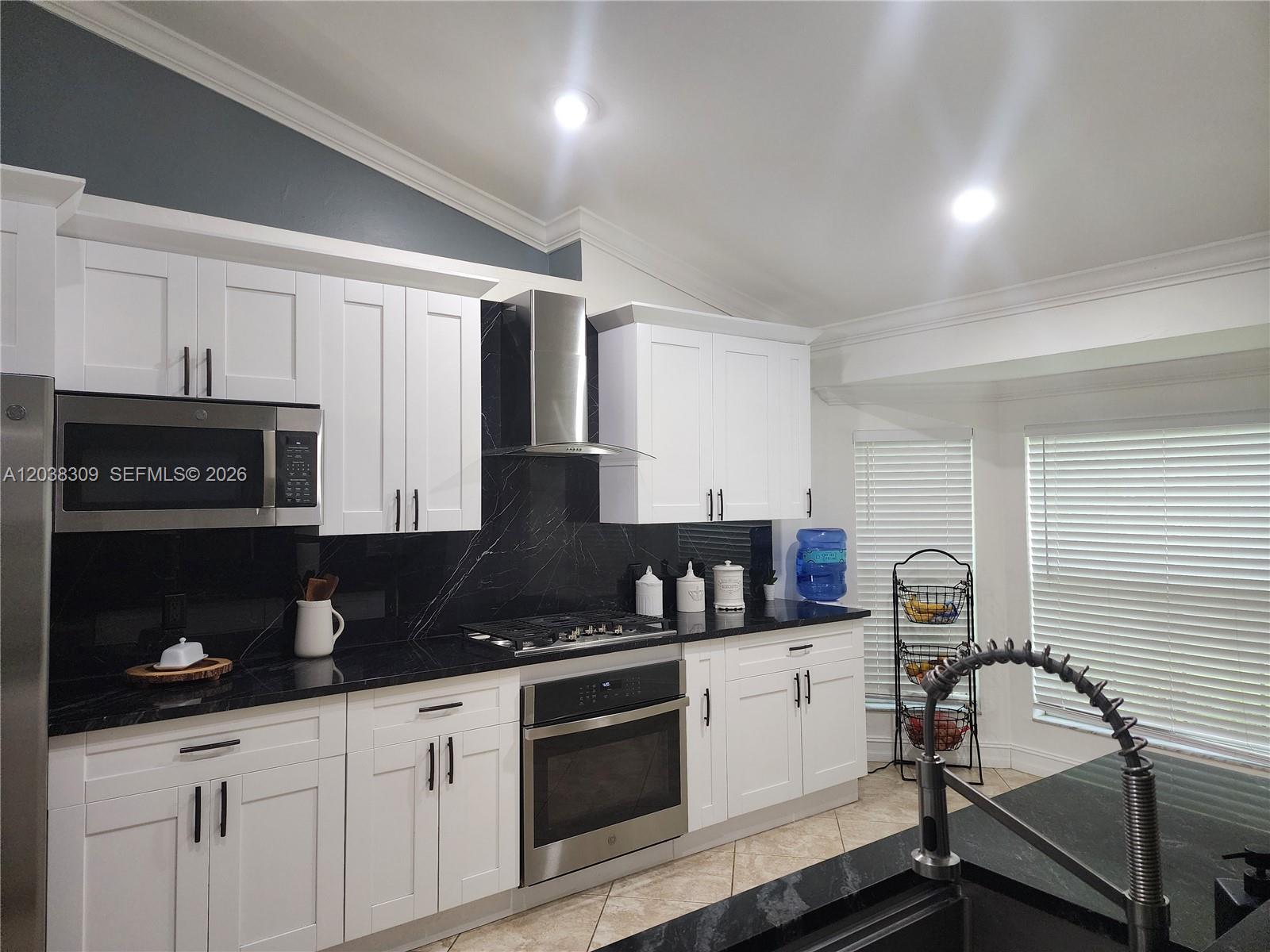 A kitchen features white cabinets, black countertops, a stainless steel oven, and a range hood — 111 2ND ST SE, Naples FL 34117, NAPLES, FL