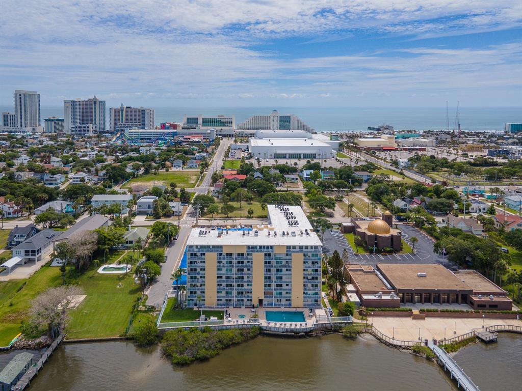 An aerial view shows a multi-story apartment building with a pool beside a body of water — 145 N HALIFAX AVENUE UNIT 711, DAYTONA BEACH, FL