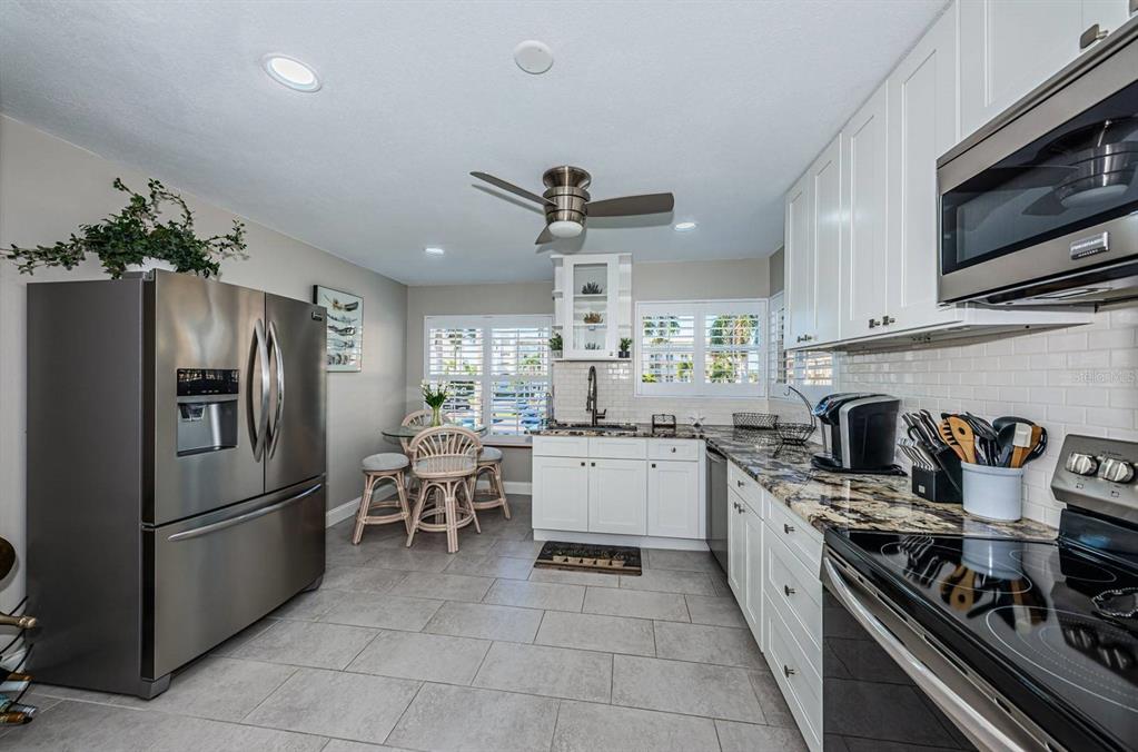 A kitchen with stainless steel appliances, white cabinets, granite countertops, and a small dining area — 6000 BAHIA DEL MAR CIRCLE UNIT 229, ST PETERSBURG, FL