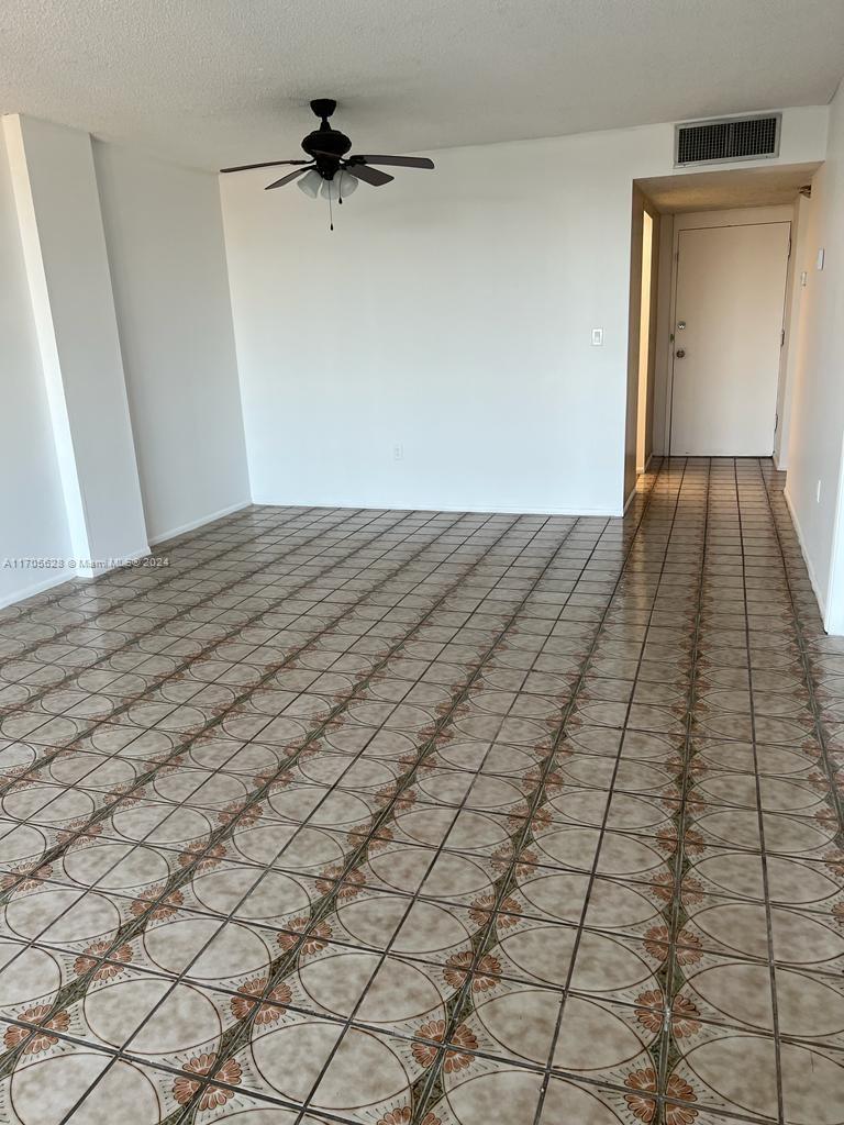 An empty room features tiled flooring, a ceiling fan, and a doorway leading to a hallway — 15600 NW 7th Ave # 821, Miami FL 33169, MIAMI, FL