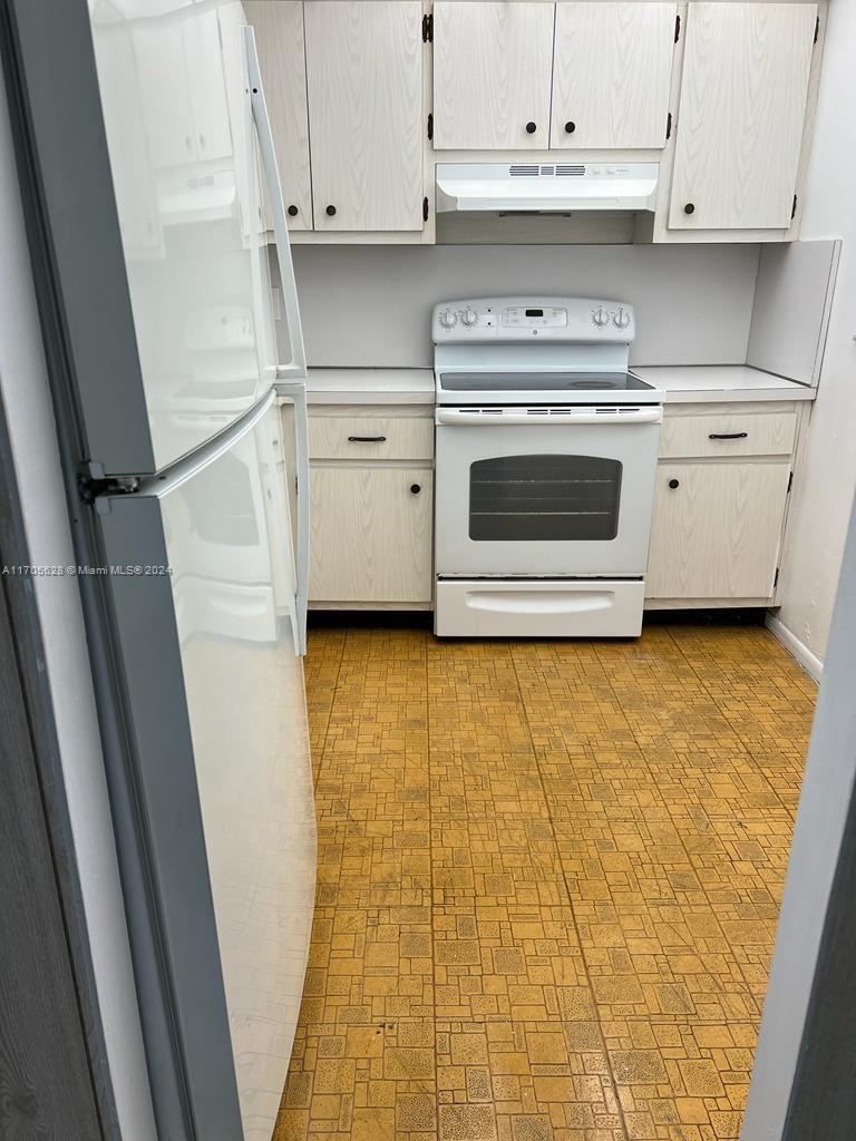 A galley kitchen features white appliances, light wood cabinets, and yellow patterned vinyl flooring — 15600 NW 7th Ave # 821, Miami FL 33169, MIAMI, FL