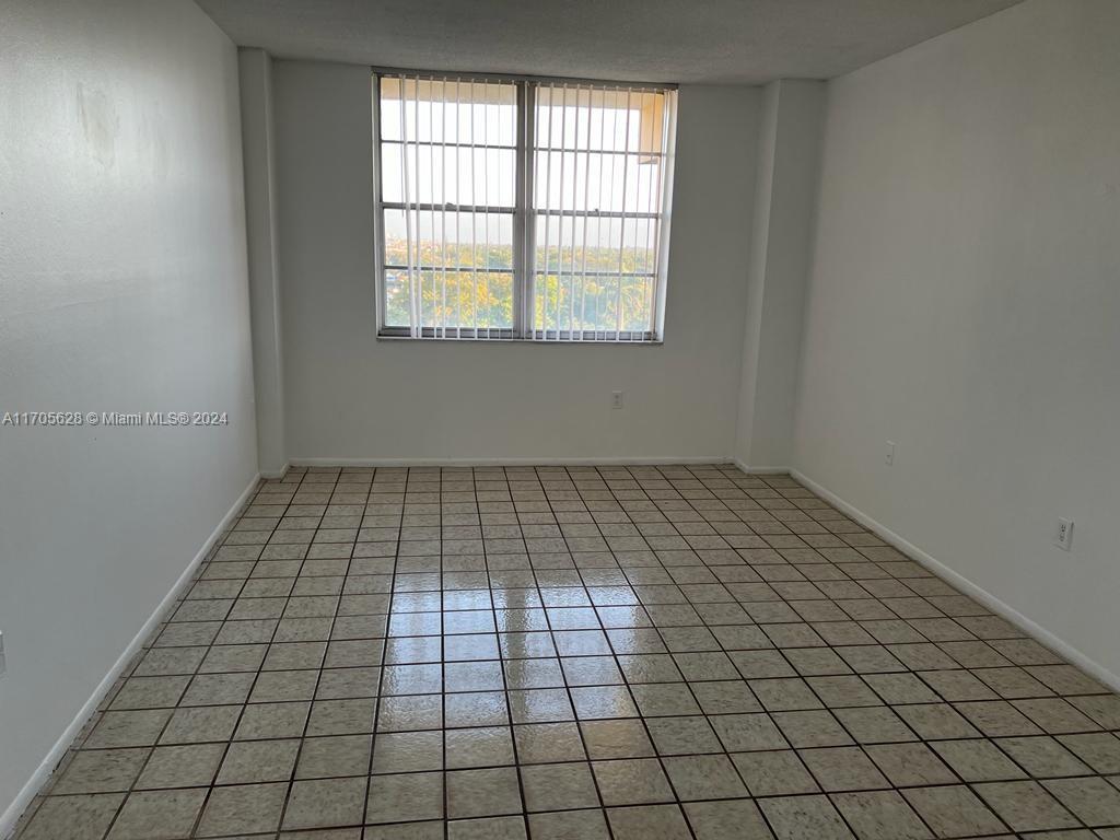 An empty room features white walls, a large window with vertical blinds, and tiled flooring — 15600 NW 7th Ave # 821, Miami FL 33169, MIAMI, FL
