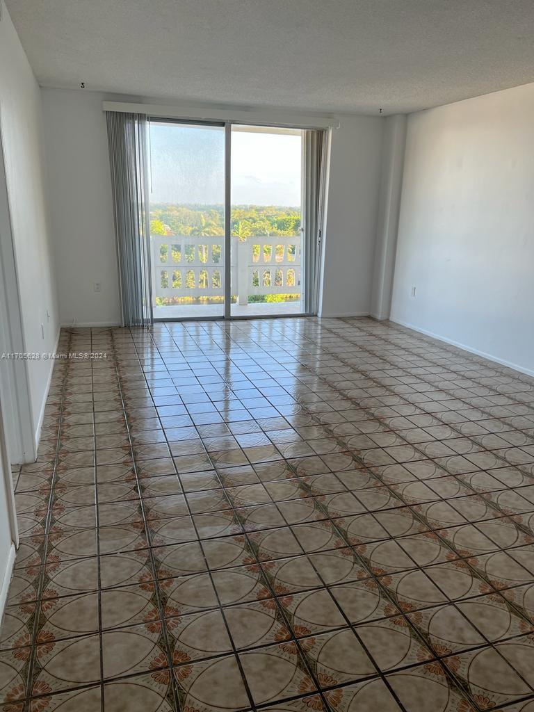 An empty room with patterned tile flooring and a sliding glass door leading to a balcony — 15600 NW 7th Ave # 821, Miami FL 33169, MIAMI, FL