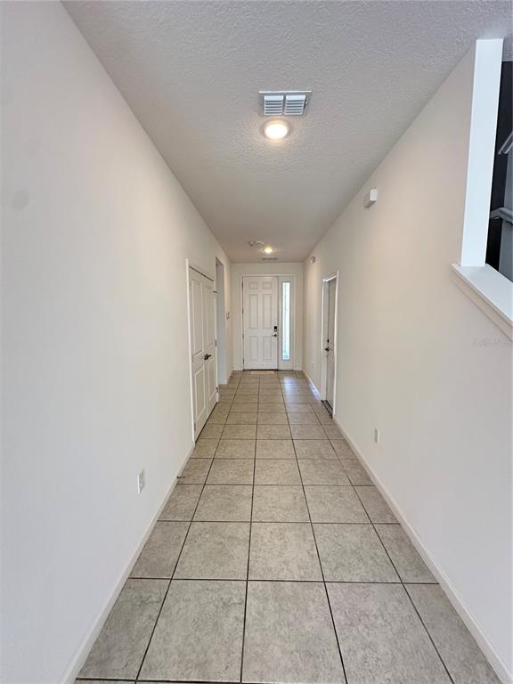 A long, tiled entryway leads to a front door with white walls and a staircase — 281 BALLO DRIVE, KISSIMMEE, FL