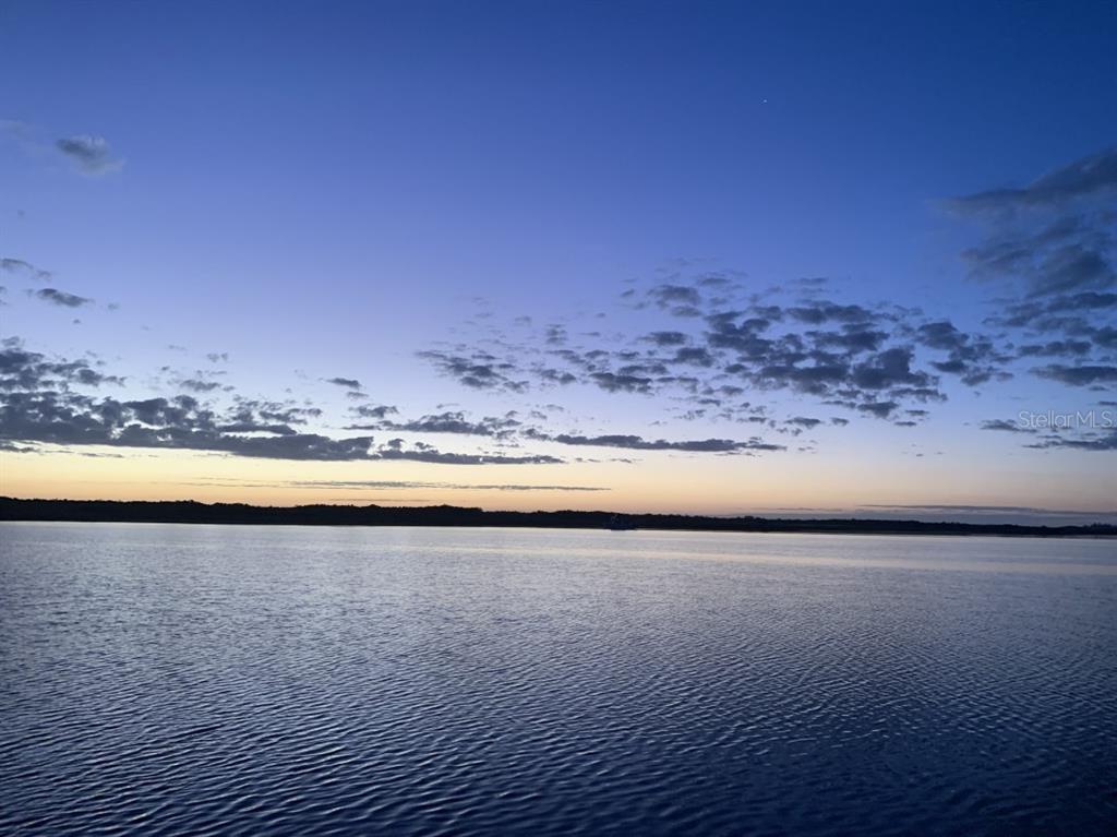 A calm lake reflects a sunset sky with scattered clouds above a distant treeline — 9488 ST MARYS COURT, PORT CHARLOTTE, FL