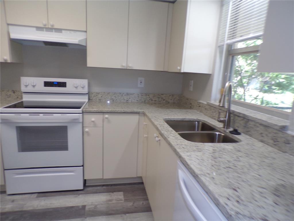 A kitchen features white cabinets, granite countertops, a white stove, and a stainless steel sink — 1088 MELVILLE ROAD UNIT A, PUNTA GORDA, FL