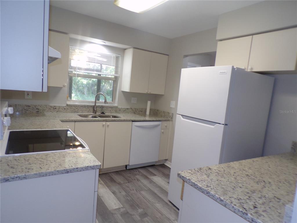 A kitchen features white cabinets, granite countertops, stainless steel sink, and light wood-look flooring — 1088 MELVILLE ROAD UNIT A, PUNTA GORDA, FL