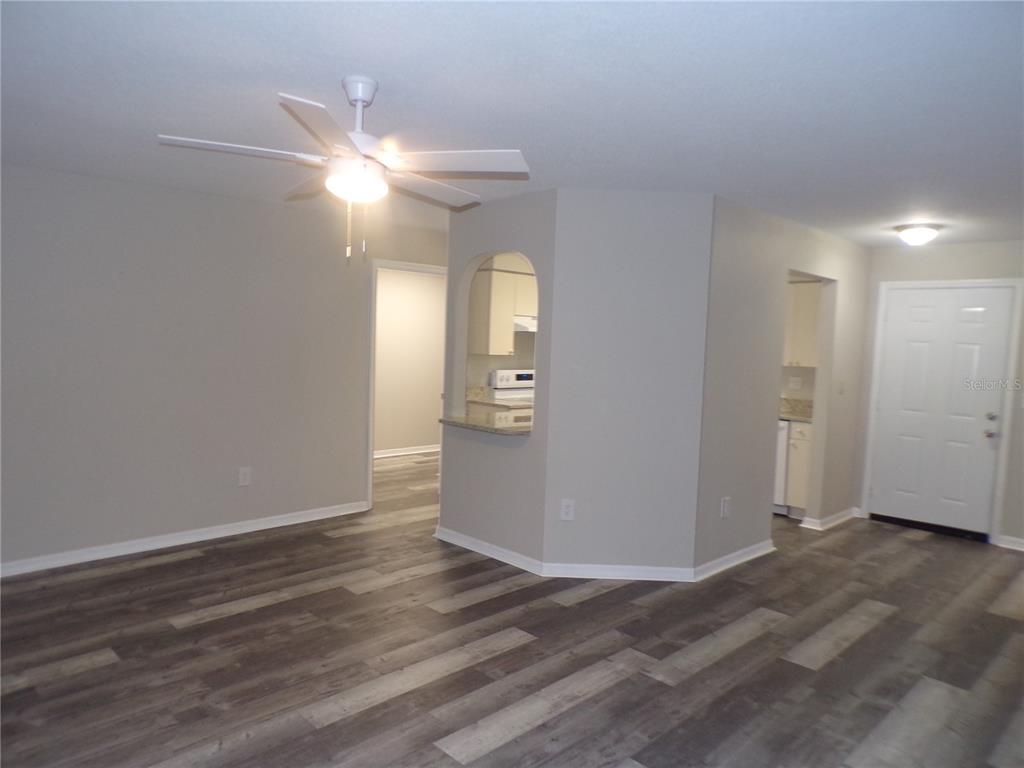 An open living area features wood-look flooring, a ceiling fan, and a kitchen pass-through window — 1088 MELVILLE ROAD UNIT A, PUNTA GORDA, FL