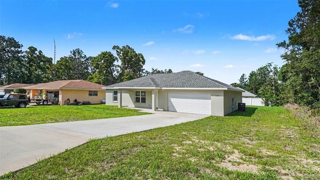 A single-story house with a white garage door and a concrete driveway under a blue sky — 5360 SW 164TH STREET ROAD, OCALA, FL