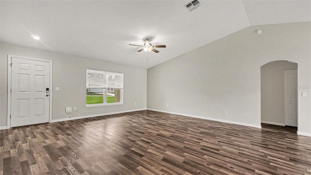 An empty living room features wood-look flooring, a vaulted ceiling with a fan, and white walls — 5360 SW 164TH STREET ROAD, OCALA, FL