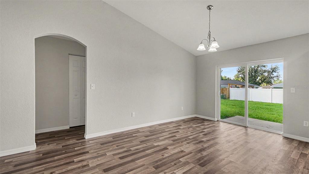 An empty room with wood-look flooring, a vaulted ceiling, a chandelier, and a sliding glass door — 5360 SW 164TH STREET ROAD, OCALA, FL