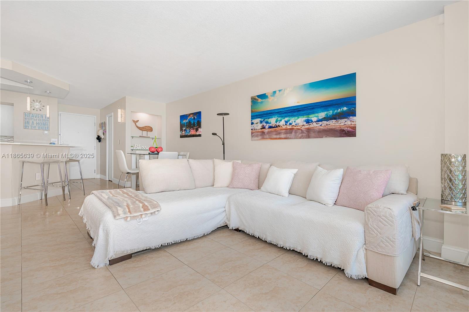 A living room features a large sectional sofa, tiled floors, and beach-themed wall art — 6917 Collins Ave # 511, Miami Beach FL 33141, MIAMI BEACH, FL
