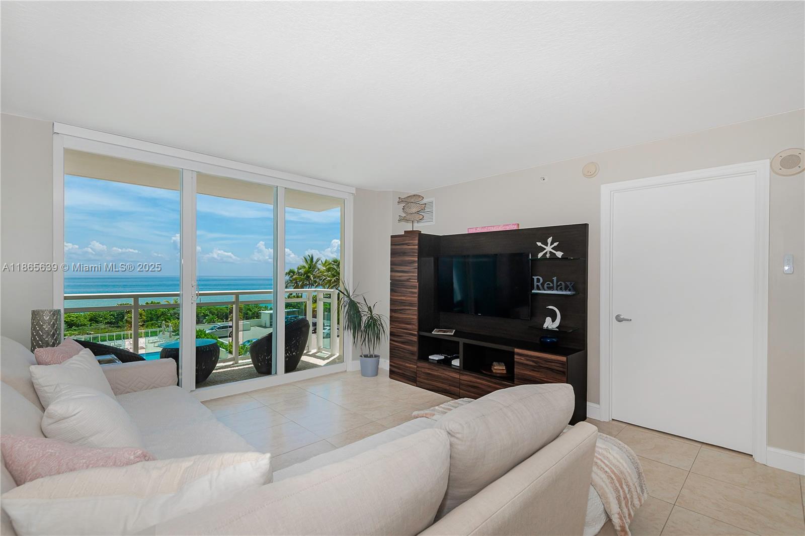 A living room features a beige sofa, a dark wood entertainment center, and a balcony view — 6917 Collins Ave # 511, Miami Beach FL 33141, MIAMI BEACH, FL