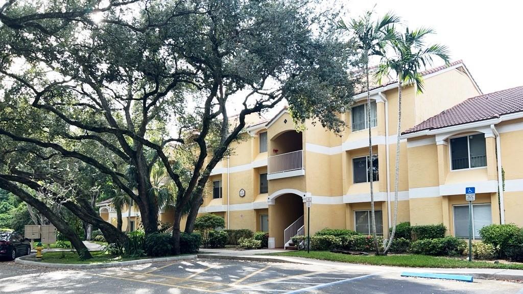 A three-story yellow apartment building stands behind a large tree and a parking lot — 2350 NW 33rd Street # 807, Oakland Park FL 33309, OAKLAND PARK, FL