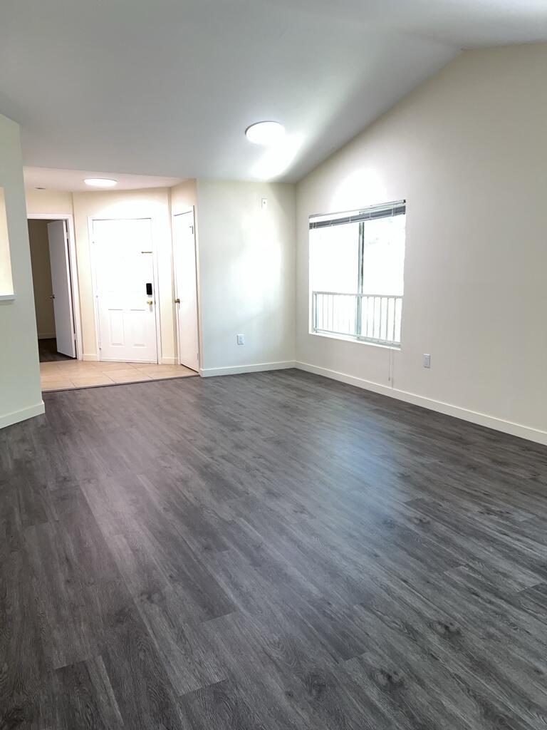 An empty living room features gray wood-look flooring, white walls, and a large window — 2350 NW 33rd Street # 807, Oakland Park FL 33309, OAKLAND PARK, FL