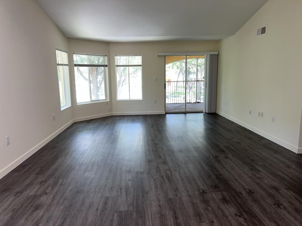 An empty living room features dark wood-look flooring, light-colored walls, multiple windows, and a sliding door — 2350 NW 33rd Street # 807, Oakland Park FL 33309, OAKLAND PARK, FL