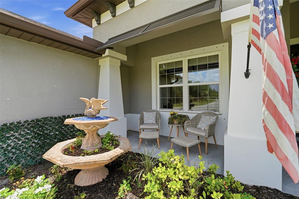 A front porch features a tiered fountain, two wicker chairs with ottomans, and an American flag — 6755 TROPICAIRE BOULEVARD, NORTH PORT, FL