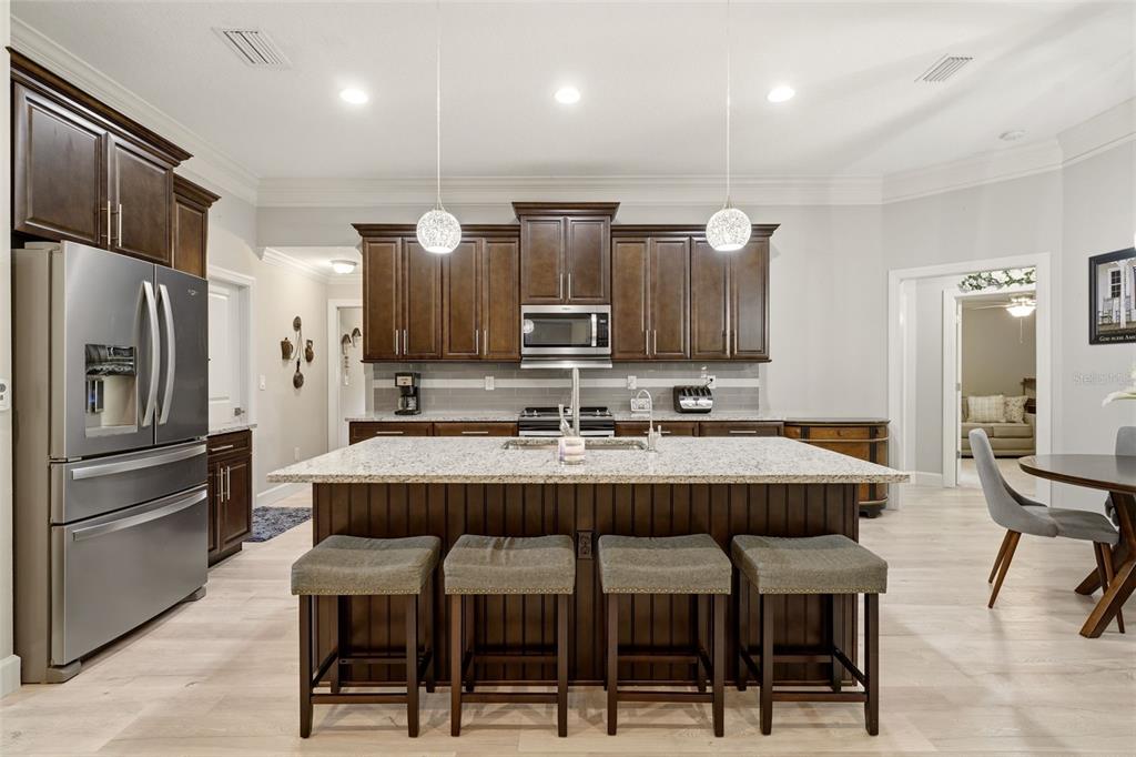A kitchen features dark wood cabinets, a granite-topped island with four stools, and stainless appliances — 6755 TROPICAIRE BOULEVARD, NORTH PORT, FL