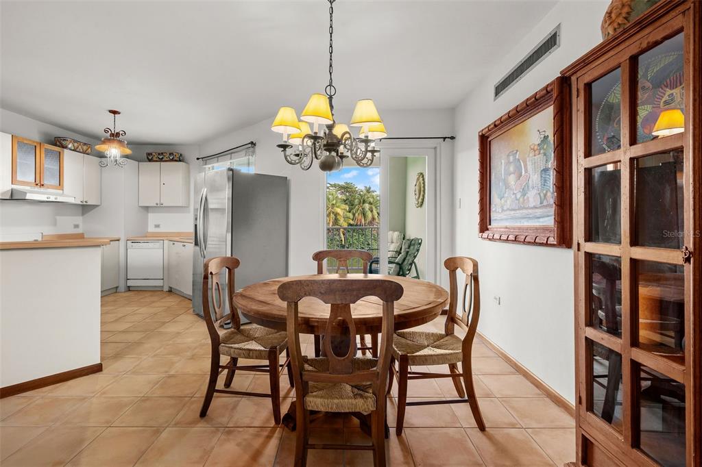 A dining area with a round wooden table, chairs, and a chandelier next to a kitchen — 195 CANDELERO DRIVE UNIT 6232, HUMACAO, PR
