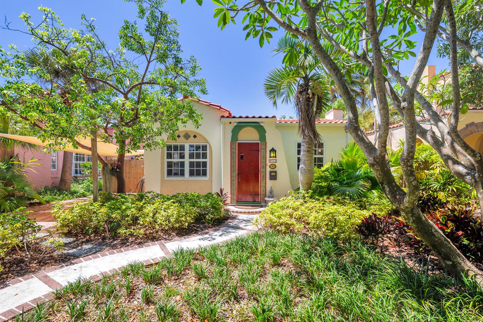 A single-story Spanish-style house with a red door, tiled roof, and lush front garden — 714 Sunset Road, West Palm Beach FL 33401, WEST PALM BEACH, FL