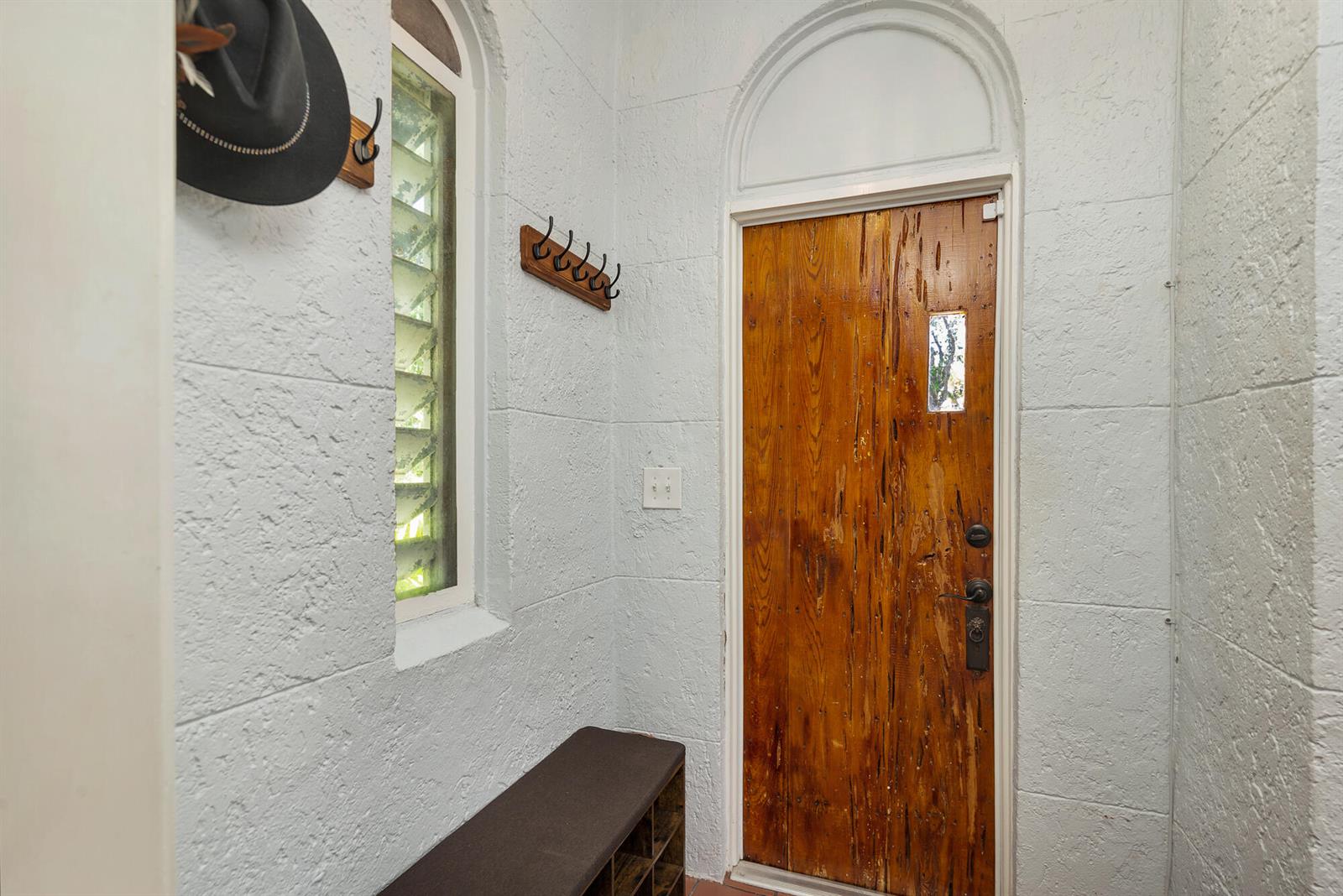 An entryway features a textured white wall, a wooden door, a bench, and wall hooks — 714 Sunset Road, West Palm Beach FL 33401, WEST PALM BEACH, FL