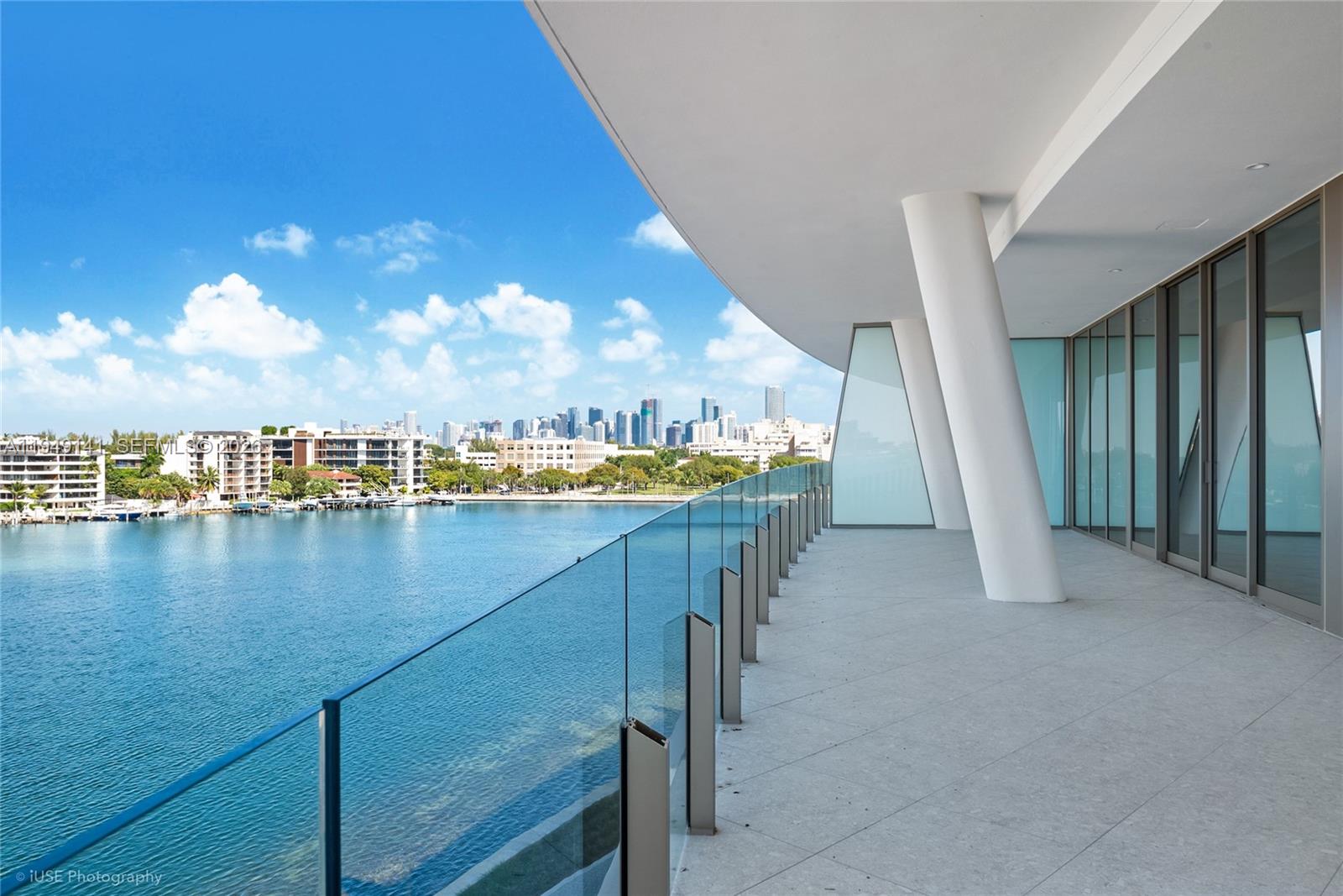 A spacious balcony with glass railings overlooks a bay and a distant city skyline — 5 Grove Isle Dr. # S503, Miami FL 33133, MIAMI, FL