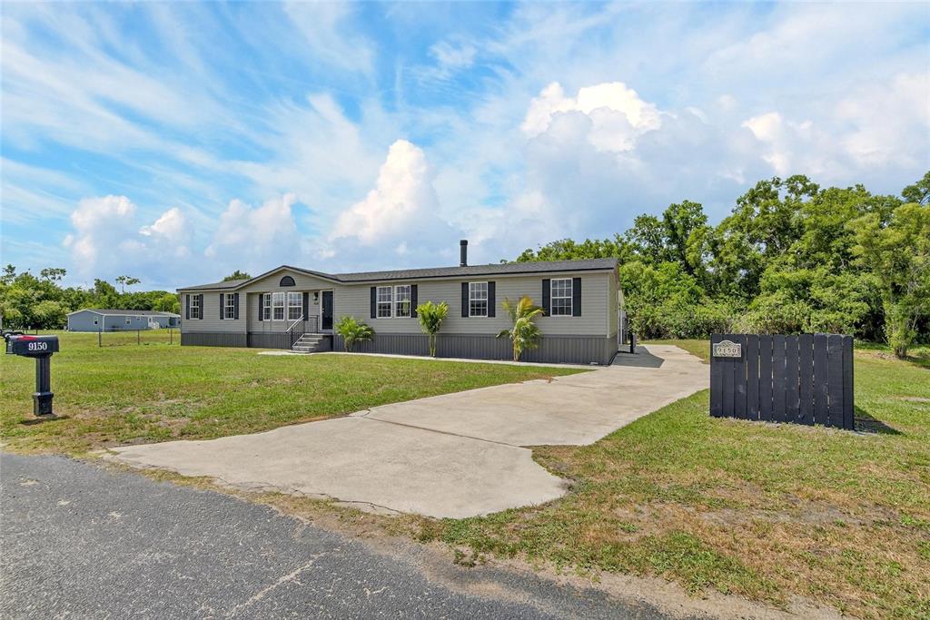 A single-story manufactured home with grey siding sits on a grassy lot with a driveway — 9150 WOOD TERRACE DRIVE, TAMPA, FL