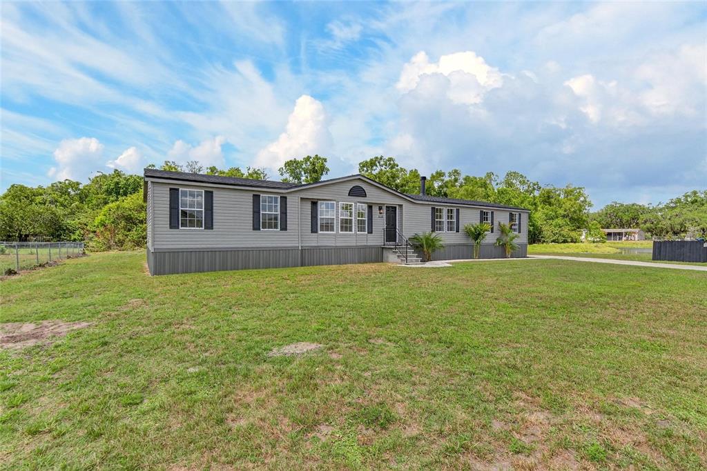 A gray manufactured home sits on a large grassy lot under a cloudy sky — 9150 WOOD TERRACE DRIVE, TAMPA, FL