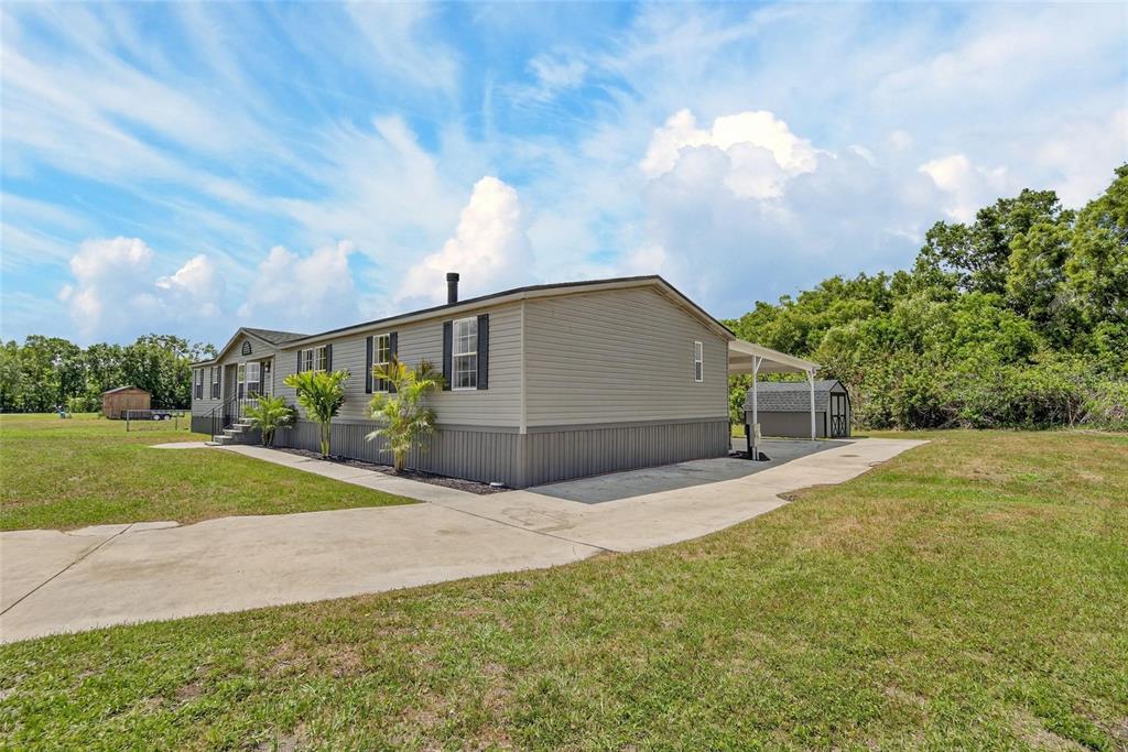 A single-story manufactured home with light siding and a concrete driveway sits on a lawn — 9150 WOOD TERRACE DRIVE, TAMPA, FL