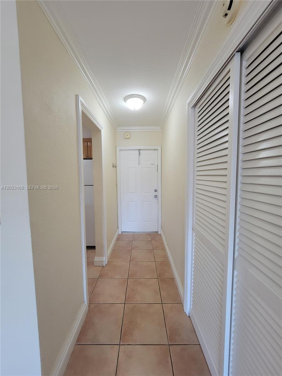 A hallway with beige walls, tile flooring, and white louvered closet doors leads to a door — 6707 N Kendall Dr # 107, Pinecrest FL 33156, PINECREST, FL
