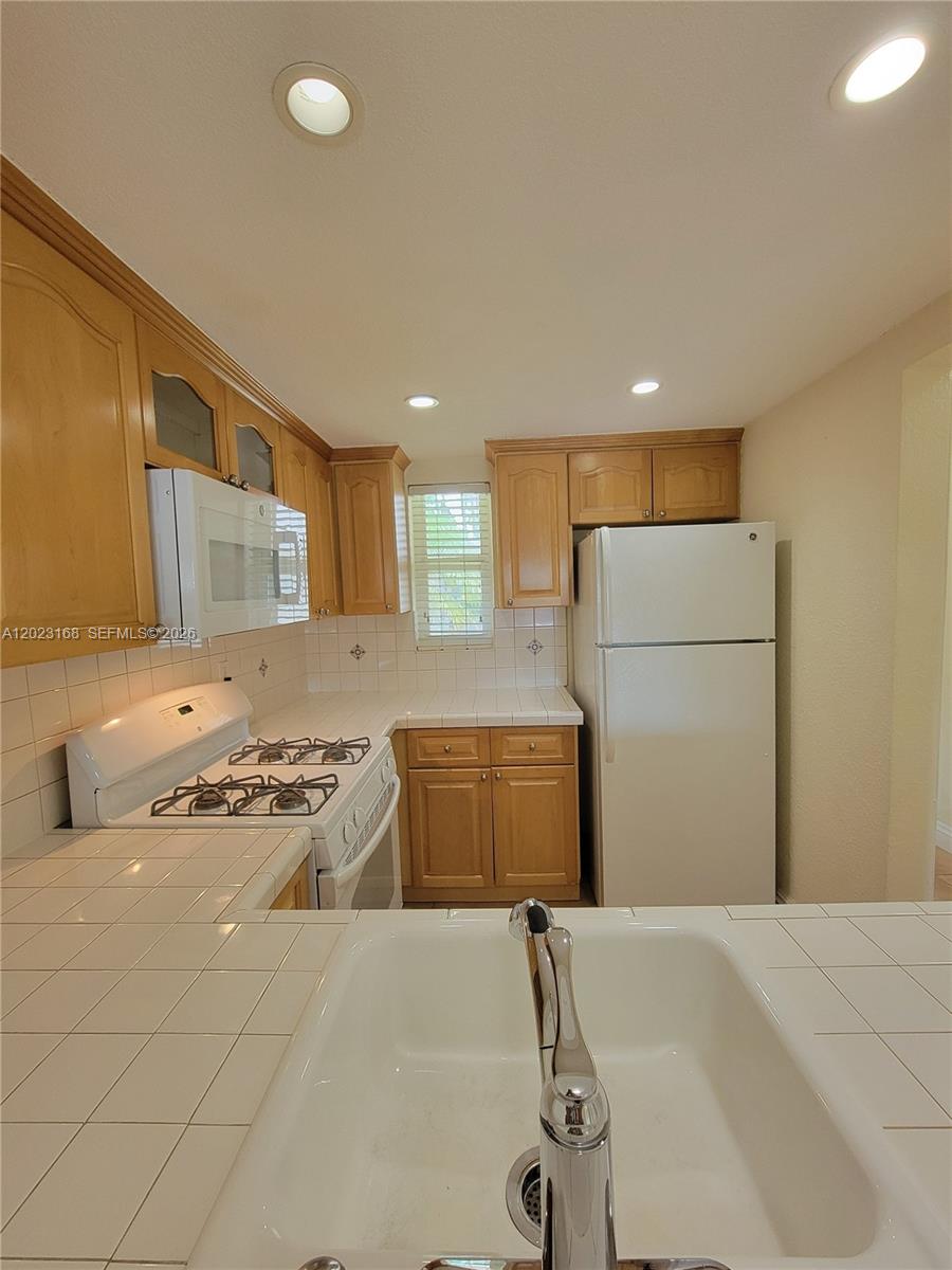 This kitchen features light wood cabinets, white tile countertops, and white appliances — 6707 N Kendall Dr # 107, Pinecrest FL 33156, PINECREST, FL