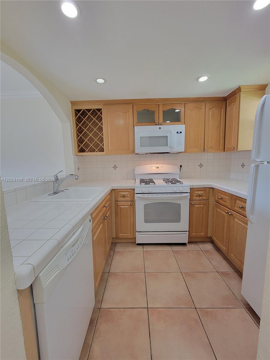 A kitchen features light wood cabinets, white tile countertops, and white appliances — 6707 N Kendall Dr # 107, Pinecrest FL 33156, PINECREST, FL