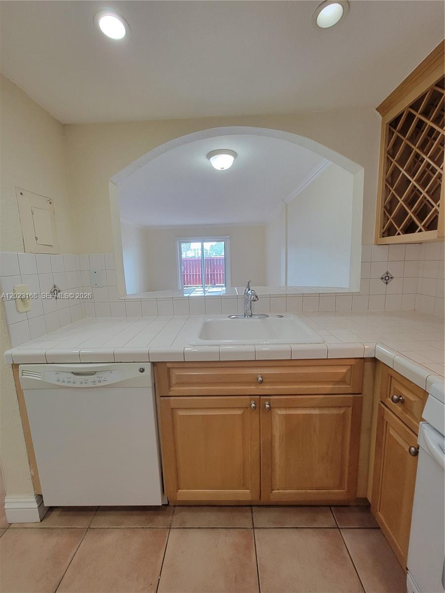 A kitchen features white tile countertops, light wood cabinets, a dishwasher, and a pass-through window — 6707 N Kendall Dr # 107, Pinecrest FL 33156, PINECREST, FL