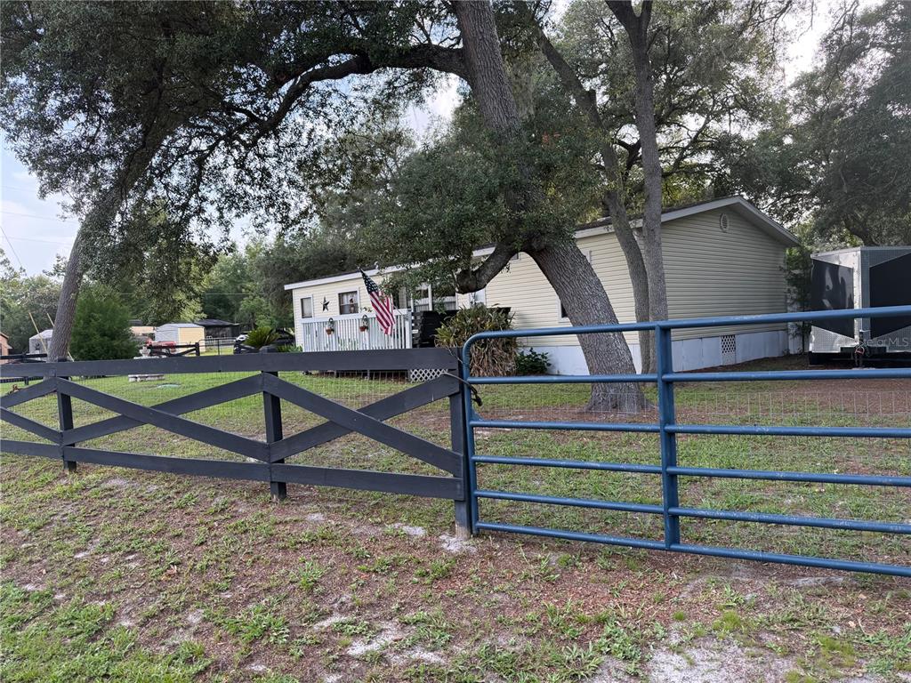 A single-story house with light siding sits behind a dark wooden and blue metal fence — 40235 OVERLOOK DRIVE, EUSTIS, FL